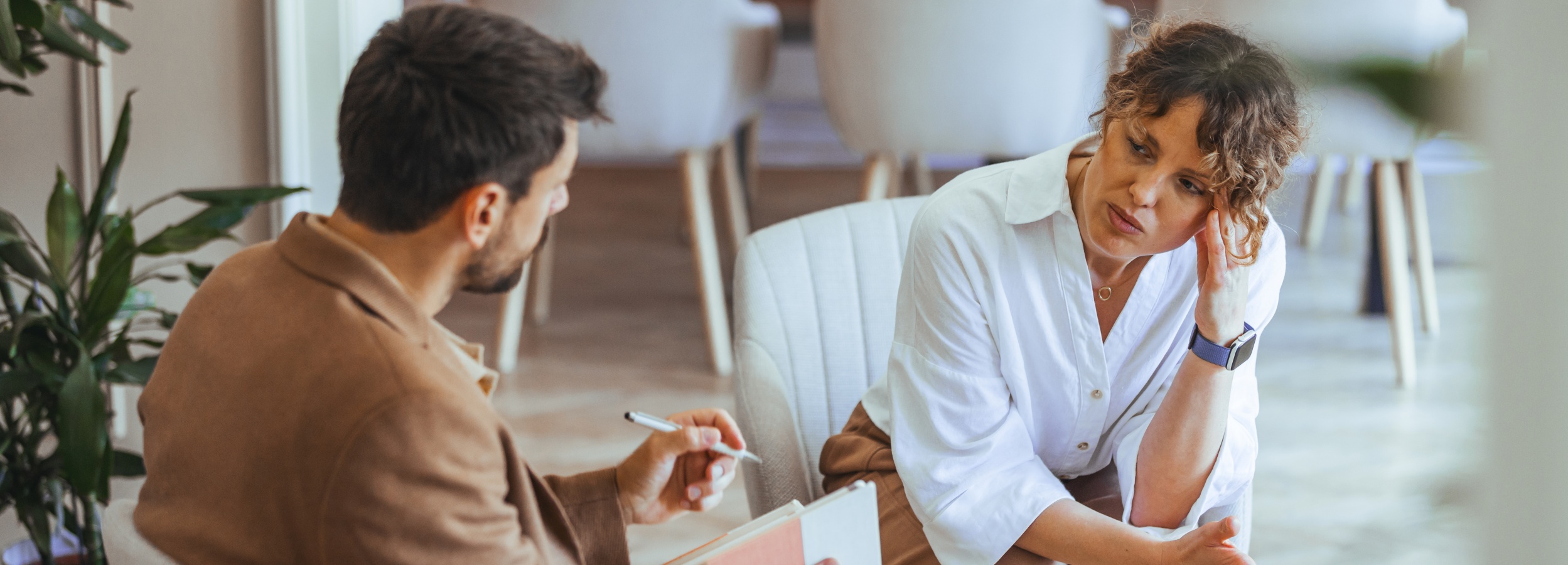 Professionelles Beratungsgespräch zwischen Thearpeut und Patienten, die in einem hellen Büro auf Stühlen gegenübersitzen.