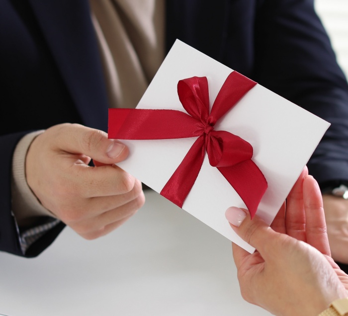 Ein Mann erhält einen Briefumschlag mit einer roten Schleife von seiner Chefin überreicht.