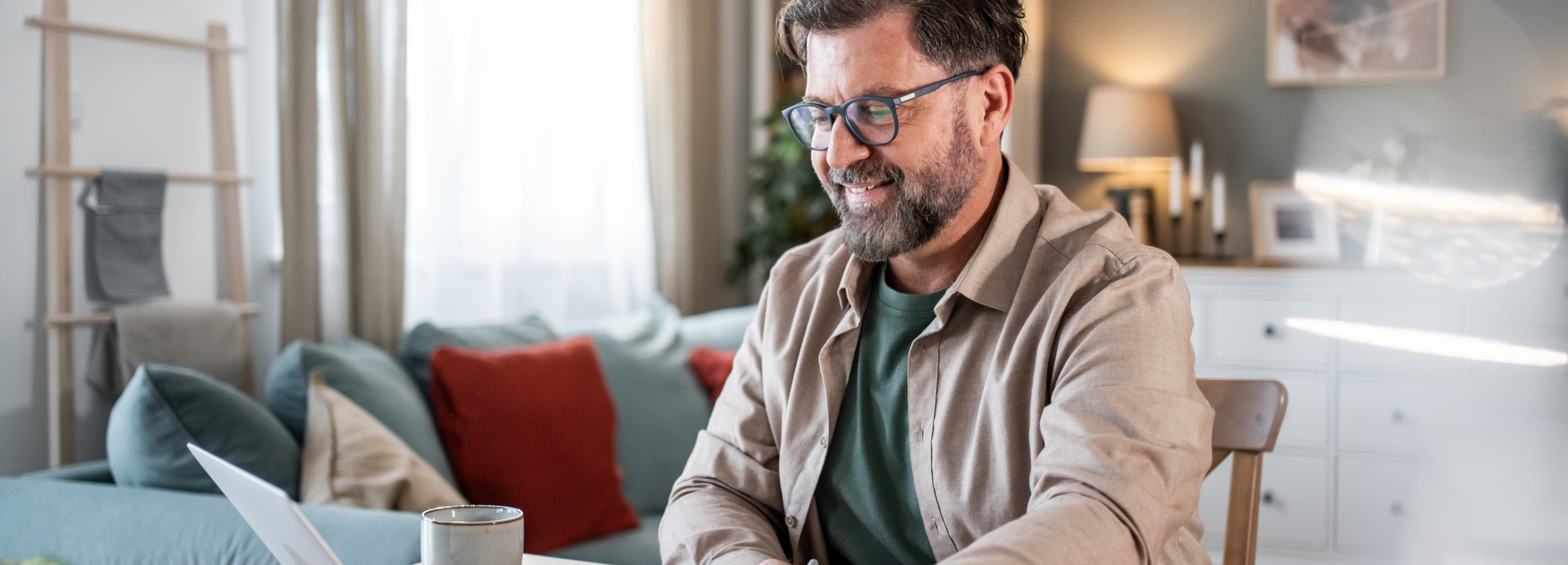 Mann mit Brille sitzt im Homeoffice lächelnd am Laptop.