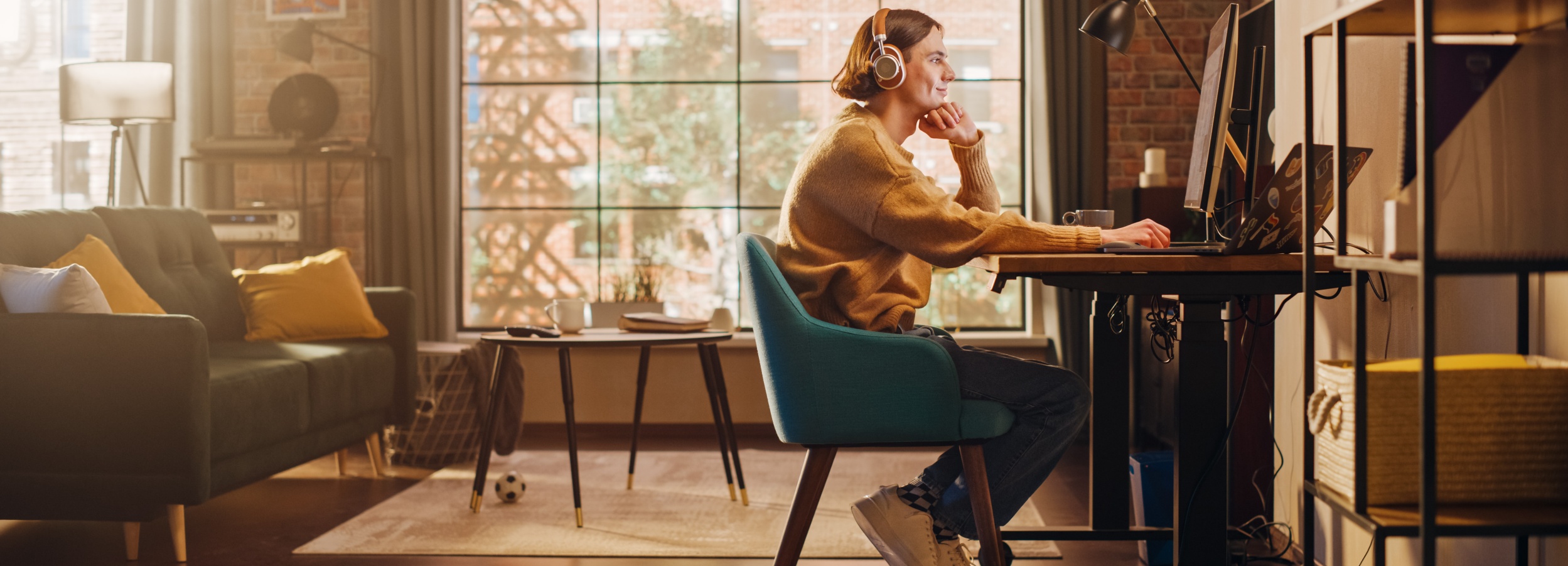 Eine Frau mit Kopfhörern sitzt in einem hellen Raum an einem Schreibtisch und arbeitet an einem Computer.